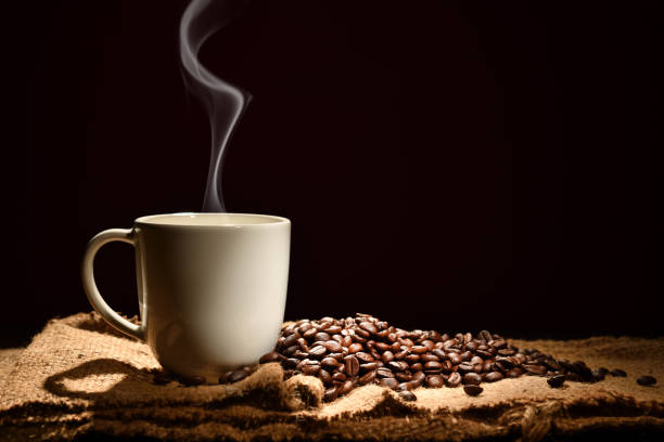 Cup of coffee with smoke and coffee beans on black background